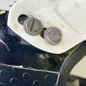 May include: Close-up of a section of a white and black motorcycle helmet. Two silver, circular screws are visible, set into the white plastic. The helmet has a black, textured section with circular indentations.