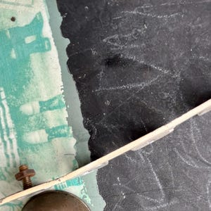 May include: A close-up of a metal bell with a white metal bracket attached to it. The bell is partially visible and the bracket is attached to a black surface.
