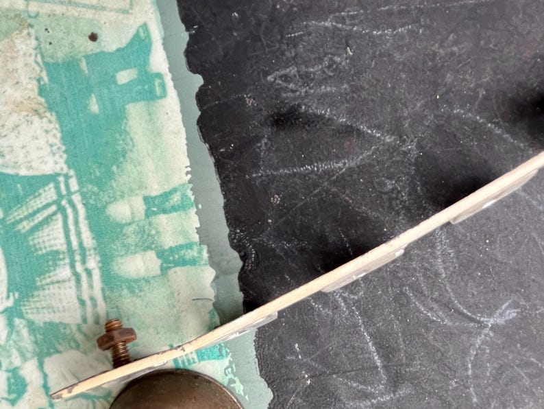 May include: A close-up of a metal bell with a white metal bracket attached to it. The bell is partially visible and the bracket is attached to a black surface.