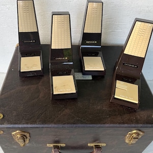 May include: Four vintage Darome Model 250 intercoms with a brown and gold color scheme. Each unit has a rectangular base with a gold-colored plate and the words "PUSH TO TALK". The intercoms are placed on a brown suitcase.