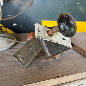 May include: A vintage door lock with a black porcelain knob, a white porcelain faceplate, and a brass keyhole. The lock is attached to a wooden surface.