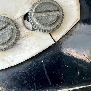 May include: Close-up of a vintage can opener. The image shows two silver, circular adjustment wheels with ridged edges and a slotted center. The can opener is set against a white and black background.