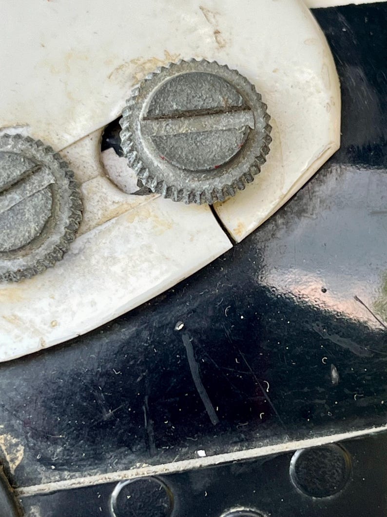 May include: Close-up of a vintage can opener. The image shows two silver, circular adjustment wheels with ridged edges and a slotted center. The can opener is set against a white and black background.