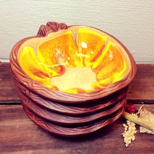 May include: A set of four ceramic bowls with a wood-grain design. The bowls are stacked on top of each other. The top bowl has a yellow and orange glaze with a marbled effect.