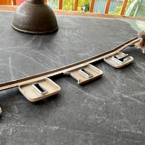 May include: A silver metal car emblem with the word "Dodge" spelled out in raised letters. The emblem has five sections with a screw in each section. The emblem is on a dark gray surface.