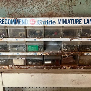 May include: A white metal drawer unit with the text "We Recommend AC Guide Miniature Lamps" on the top. The drawers are labeled with numbers and contain various small parts.