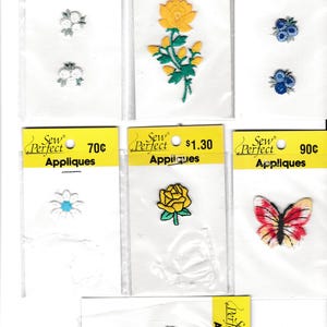 May include: Assortment of iron-on appliques for sewing projects. The appliques include a yellow rose, a butterfly, a daisy, blueberries, and a floral design. The appliques are packaged on cards with the price and the brand name "Sew Perfect".