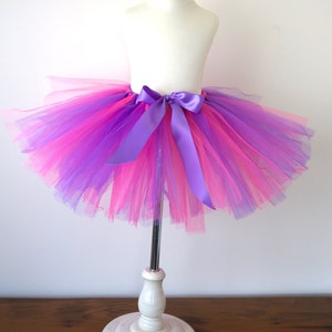 May include: A pink and purple tulle tutu with a purple satin ribbon tied around the waist.