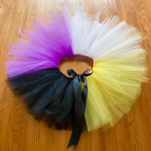 May include: A multi-colored tulle skirt with black, purple, white, and yellow sections. The skirt is tied with a black ribbon.