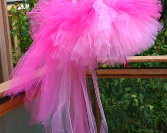 May include: A pink tulle tutu with a long train. The tutu is layered and has a gradient from dark pink to light pink.