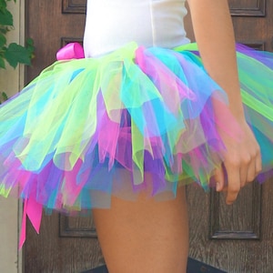 Puede incluir: Una falda de tut&uacute; de tul multicolor con una cinta rosa. La falda est&aacute; compuesta por capas de tul verde, azul, morado y rosa.