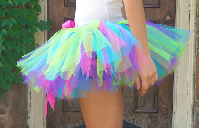 Puede incluir: Una falda de tut&uacute; de tul multicolor con una cinta rosa. La falda est&aacute; compuesta por capas de tul verde, azul, morado y rosa.