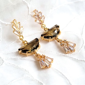 May include: A pair of gold earrings with a brown teardrop-shaped crystal and a cluster of clear crystals dangling below.