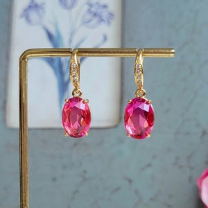 May include: A pair of gold earrings with pink oval-shaped gemstones. The earrings have a simple design and are perfect for everyday wear.