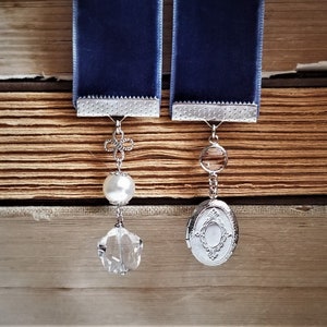 May include: Two blue velvet ribbon bookmarks with silver charms. One charm is a pearl and crystal pendant, the other is a silver locket with a crystal.