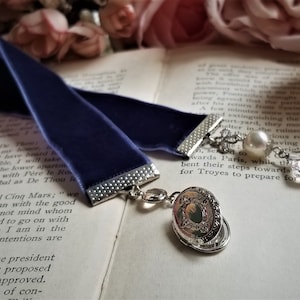 May include: A dark blue velvet bookmark with a silver chain and charm. The charm features a pearl and a crystal. The bookmark is lying on a book with text.
