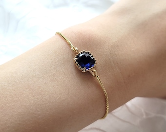 Peut inclure: Un bracelet en chaîne dorée avec une pierre précieuse bleu foncé dans un sertissage en or. Le bracelet est réglable.