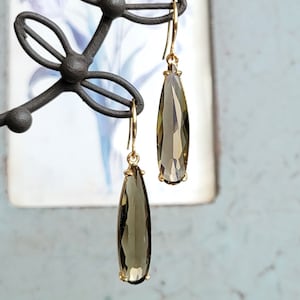May include: A pair of gold dangle earrings with teardrop-shaped smoky quartz stones.