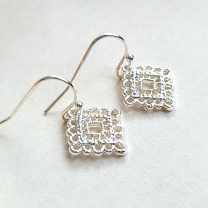 Puede incluir: Un par de pendientes de plata con un delicado diseño intrincado en forma de diamante. Los pendientes tienen un cierre simple de gancho.