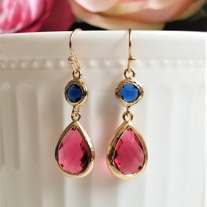 May include: Gold dangle earrings with a teardrop-shaped pink crystal and a round blue crystal.