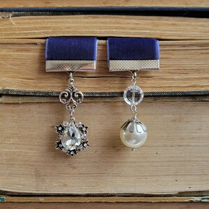 May include: Two silver bookmark charms with blue velvet ribbon accents. One charm features a teardrop-shaped crystal and the other a pearl.