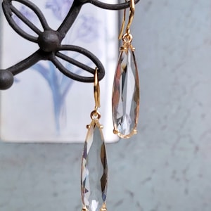 Peut inclure: Une paire de boucles d'oreilles en forme de goutte d'or avec des pierres de cristal facettées transparentes.