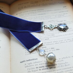 May include: A blue velvet bookmark with a silver charm and a pearl bead. The charm features a silver filigree design and a clear crystal.