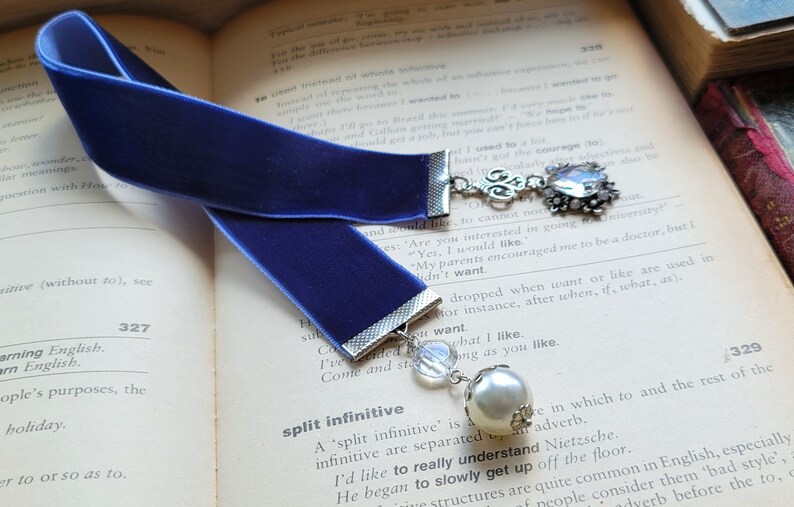 May include: A blue velvet bookmark with a silver charm and a pearl bead. The charm features a silver filigree design and a clear crystal.
