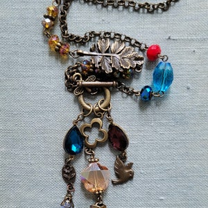 May include: A bronze chain necklace with a leaf charm, a red bead, blue beads, and a variety of crystal and glass beads hanging from the bottom.