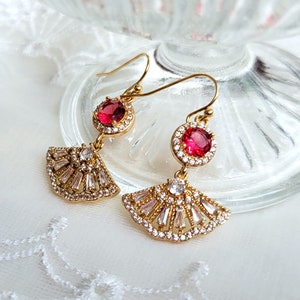 May include: Gold earrings with a fan-shaped design and red crystal accents.