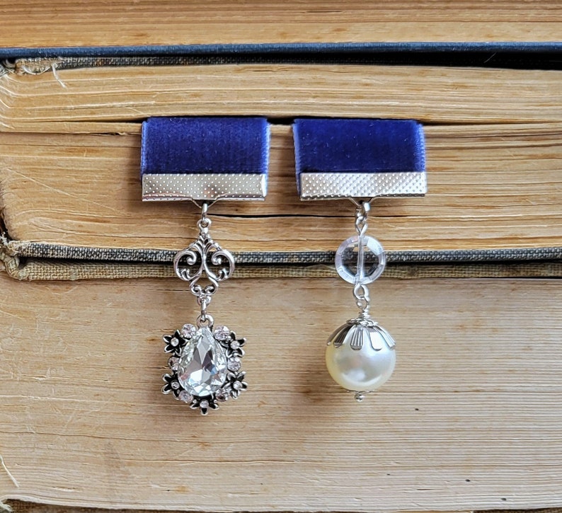 May include: Two blue velvet ribbon bookmarks with silver accents. One bookmark features a teardrop-shaped crystal pendant, the other a pearl pendant.