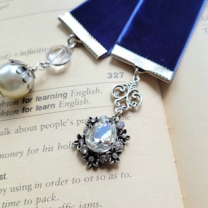 May include: A blue velvet ribbon bookmark with silver accents and crystal embellishments. The bookmark is attached to a book with the page number 327 visible.