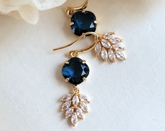 May include: A pair of gold earrings with a dark blue gemstone and a cluster of clear rhinestones hanging from each earring.