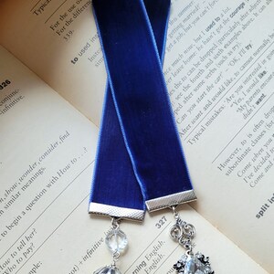 May include: A blue velvet bookmark with silver metal accents and crystal embellishments. The bookmark has the text "I went to Brighton for learn English." printed on it.