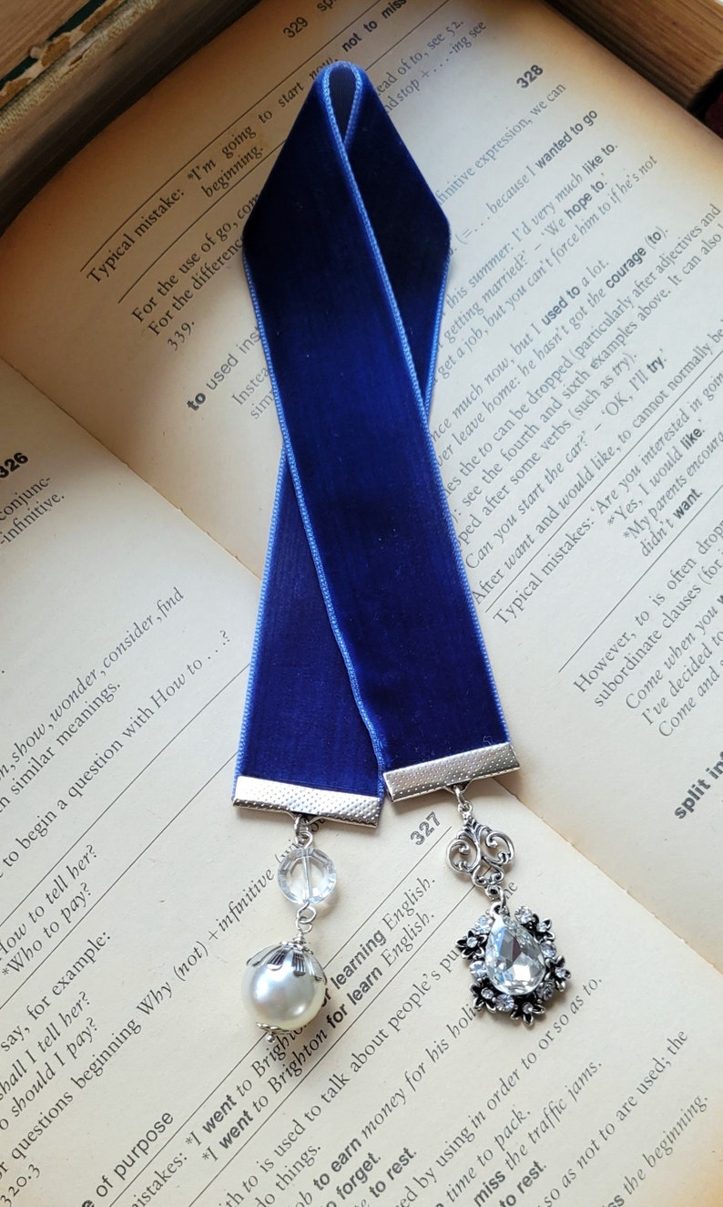 May include: A blue velvet bookmark with silver metal accents and crystal embellishments. The bookmark has the text "I went to Brighton for learn English." printed on it.