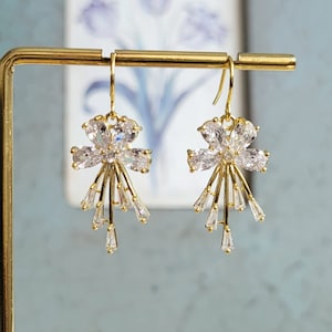 Puede incluir: Un par de pendientes de oro con un diseño floral. Cada pendiente presenta un racimo de cristales transparentes en forma de flor con detalles de cristal colgantes.