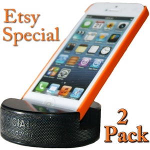 May include: Two black hockey pucks with a white "OFFICIAL" inscription. An orange iPhone case with a white iPhone is resting on the pucks. The text "Etsy Special" is in orange at the top of the image. The text "2 Pack" is in orange at the bottom of the image.