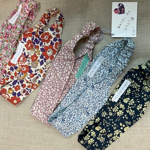 May include: A collection of floral patterned headbands in various colors, including pink, red, blue, and navy. Each headband features a fabric label with the text "SOLYIIH Designs". The headbands are displayed on a neutral linen surface.