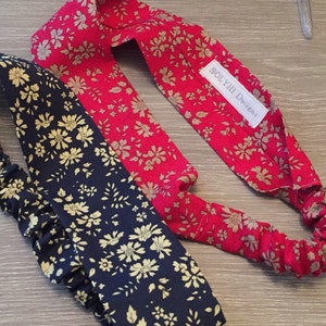 May include: Two floral headbands, one red and one navy, are displayed on a wooden surface. The red headband features a beige floral pattern, while the navy headband has a similar beige floral design. The headbands are elasticated.