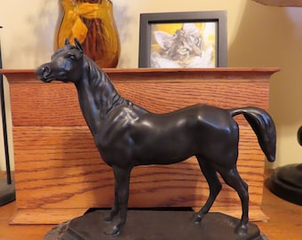 May include: A black bronze sculpture of a horse on a marble base. The horse is standing with its head held high and its tail flowing behind it.