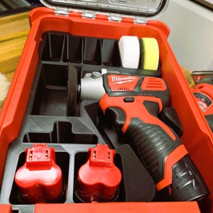 May include: A red Milwaukee power tool kit with a black handle, two red batteries, and polishing pads. The kit is open, revealing the tools and accessories inside. The Milwaukee logo is visible on the tool.