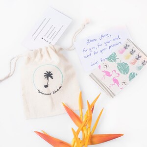 May include: A small white drawstring bag with a palm tree logo and the text "Bahamas Vintage" printed on it. A handwritten note with the text "Dear Mom, For you, for your soul and for your passion Love from" is next to the bag. A bright orange flower is in the bottom right corner of the image.