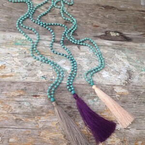 May include: Three turquoise beaded necklaces with tassels. The tassels are gray, purple, and pink.