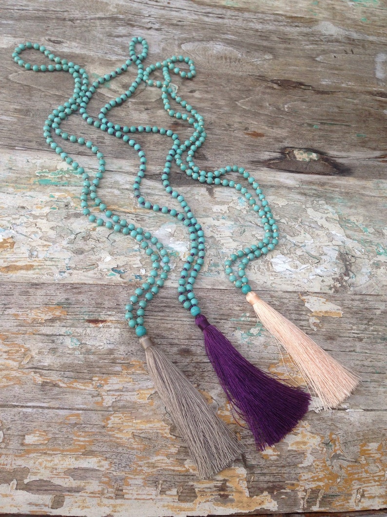 May include: Three turquoise beaded necklaces with tassels. The tassels are gray, purple, and pink.