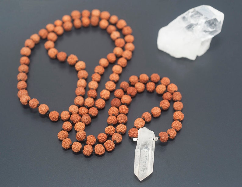 May include: A brown mala necklace with a clear quartz crystal pendant. The necklace is made of 108 beads and is strung on a black cord. The quartz crystal is a point shape and is about 2 inches long.