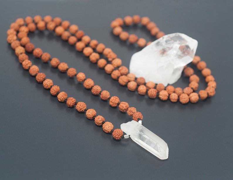 May include: A brown mala bead necklace with a clear quartz crystal pendant and a larger clear quartz crystal resting on the necklace.