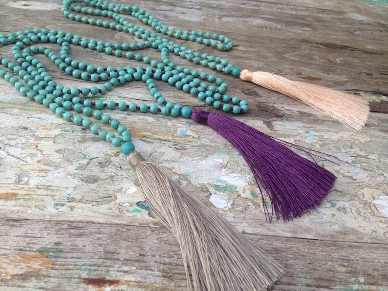 May include: Three turquoise beaded necklaces with tassels. The tassels are beige, purple, and light pink.