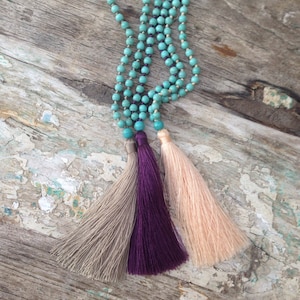 May include: A turquoise beaded necklace with three tassels, one beige, one purple, and one peach.