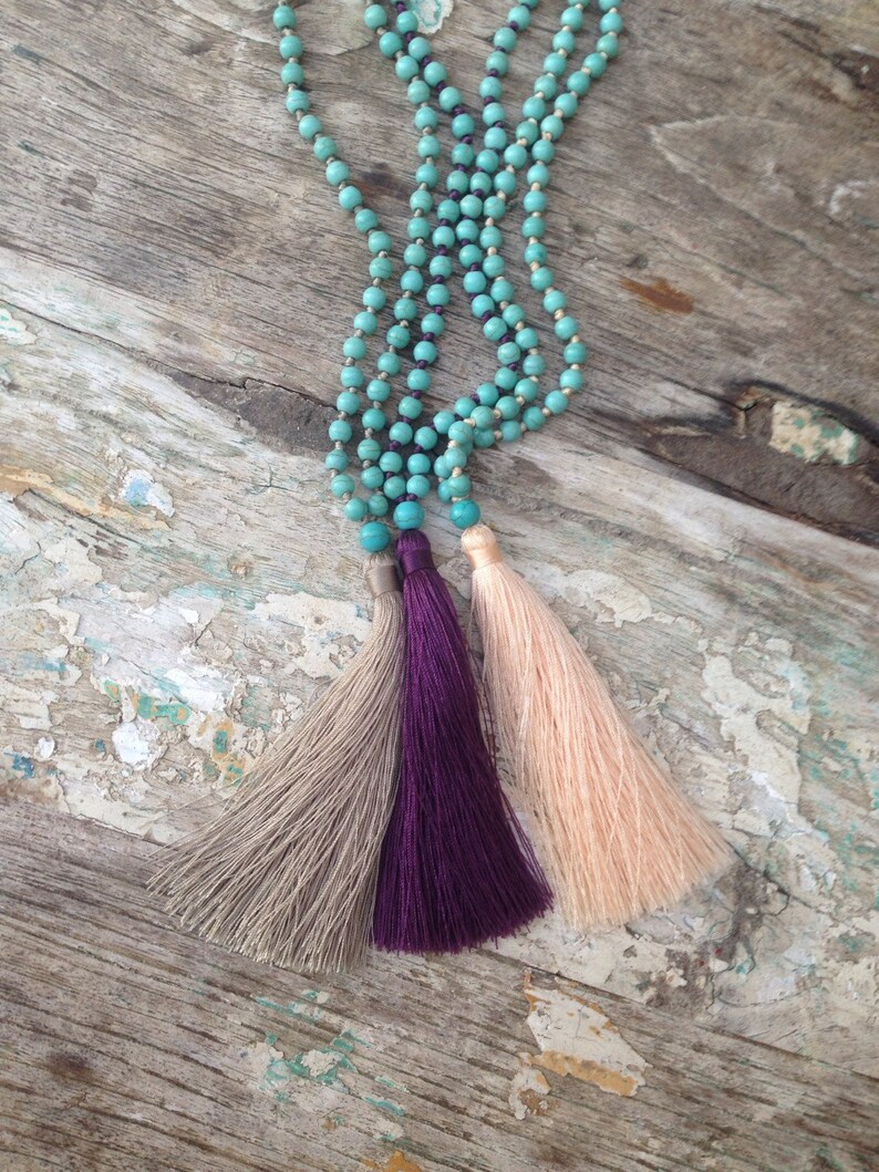May include: A turquoise beaded necklace with three tassels, one beige, one purple, and one peach.