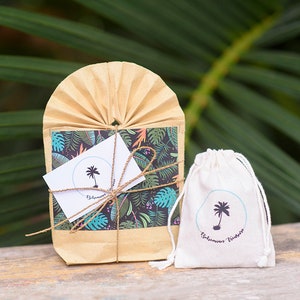 May include: A small brown paper bag with a tropical print and a white card with a palm tree logo that says "Bohemian Vibes". The bag is tied with twine and is sitting on a wooden surface. Next to the bag is a small white drawstring bag with the same palm tree logo and the text "Bohemian Vibes".
